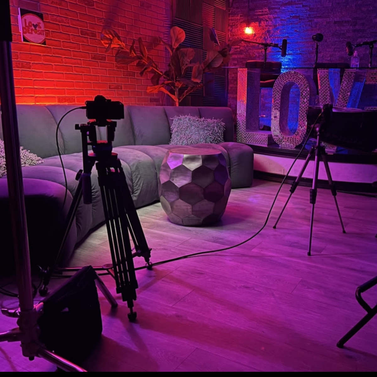 A studio setup featuring a gray sofa, a geometric table, and colorful lighting around a large "LOVE" sign.