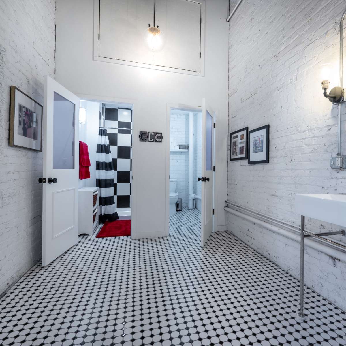 A modern bathroom with white brick walls, checkered black and white tiled floor, and a sleek sink with a mirror, leading to multiple doorways.