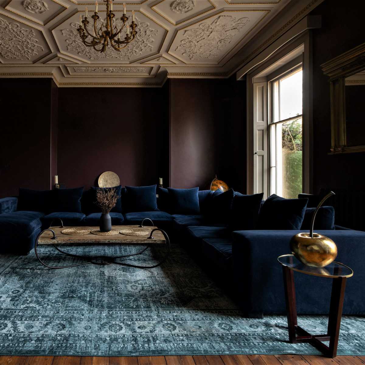 A spacious living room featuring a large dark blue sectional sofa, a round coffee table, and ornate ceiling details.