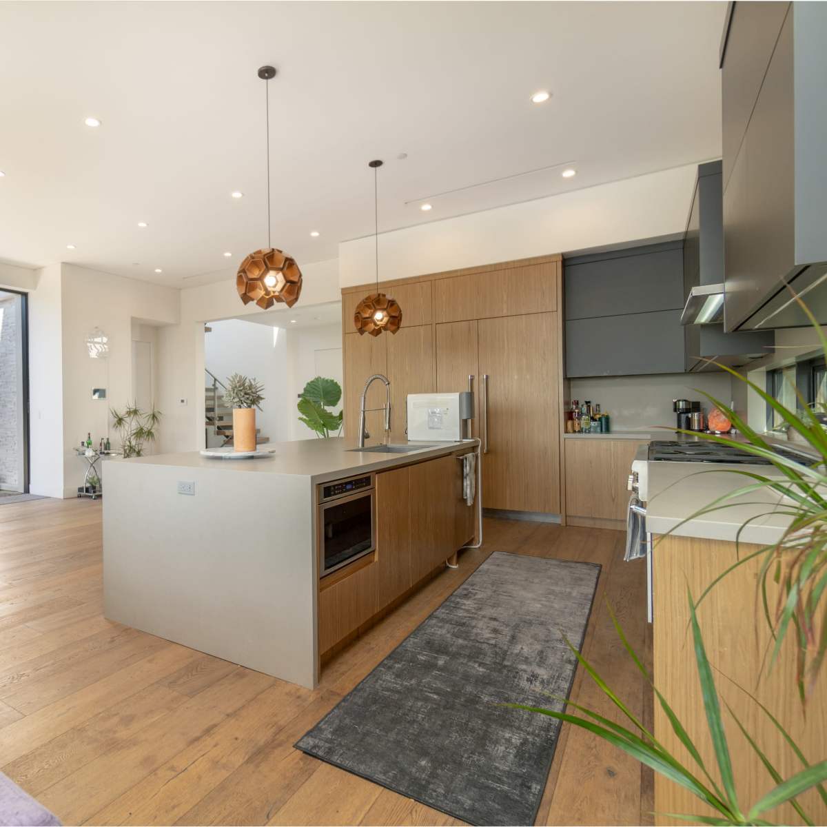 A modern kitchen with wood cabinetry, an island with seating, and large windows that open to an outdoor space.