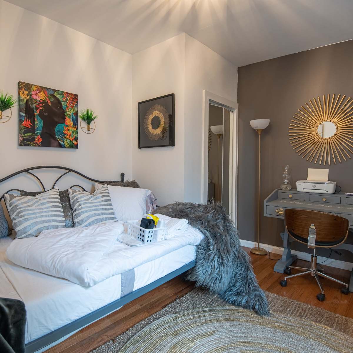 A cozy bedroom with a bed adorned in white linens, a work desk beside it, and decorative elements on the walls.