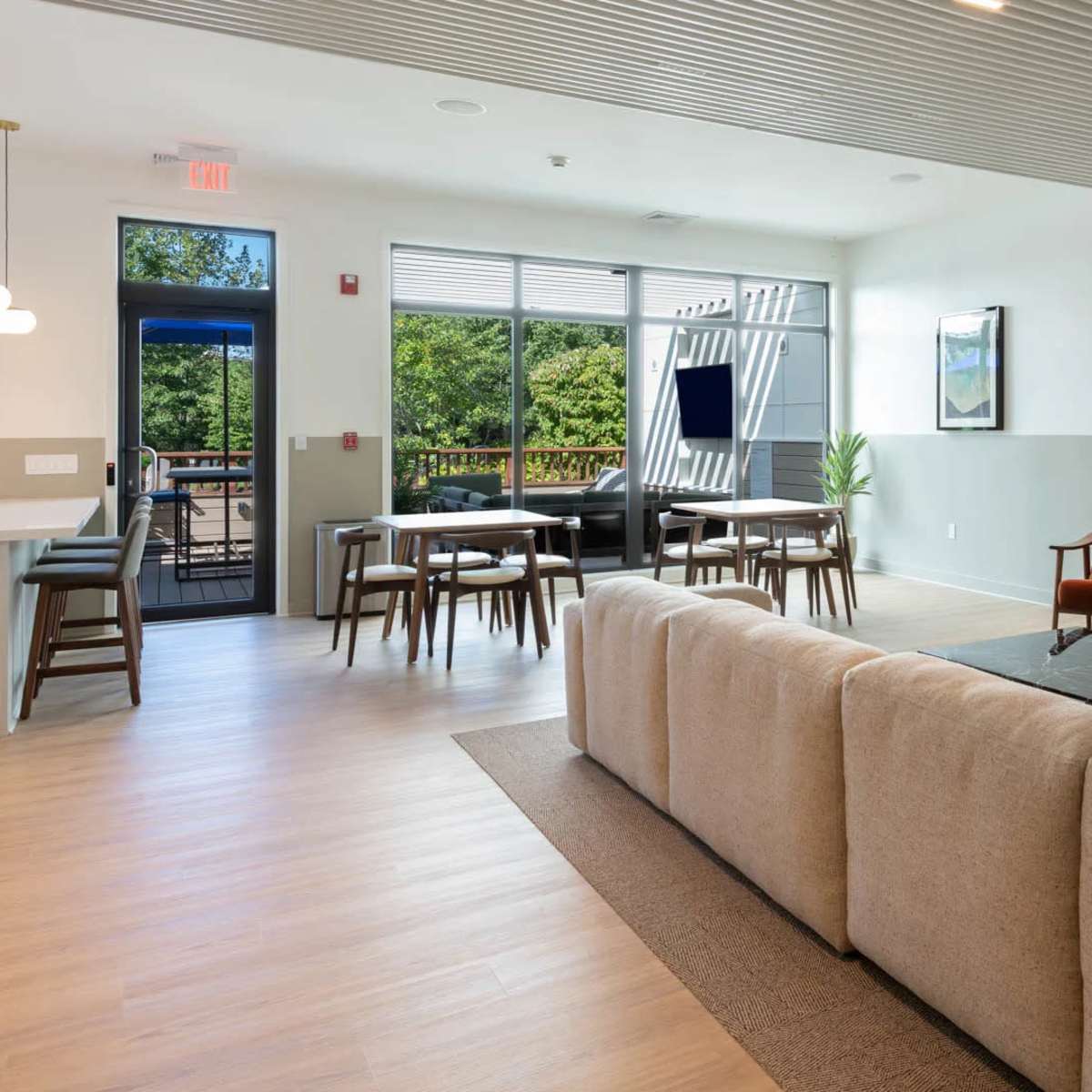 A modern lounge area featuring a large sectional sofa, a coffee table, and multiple seating arrangements, with a view of an outdoor space through large windows.