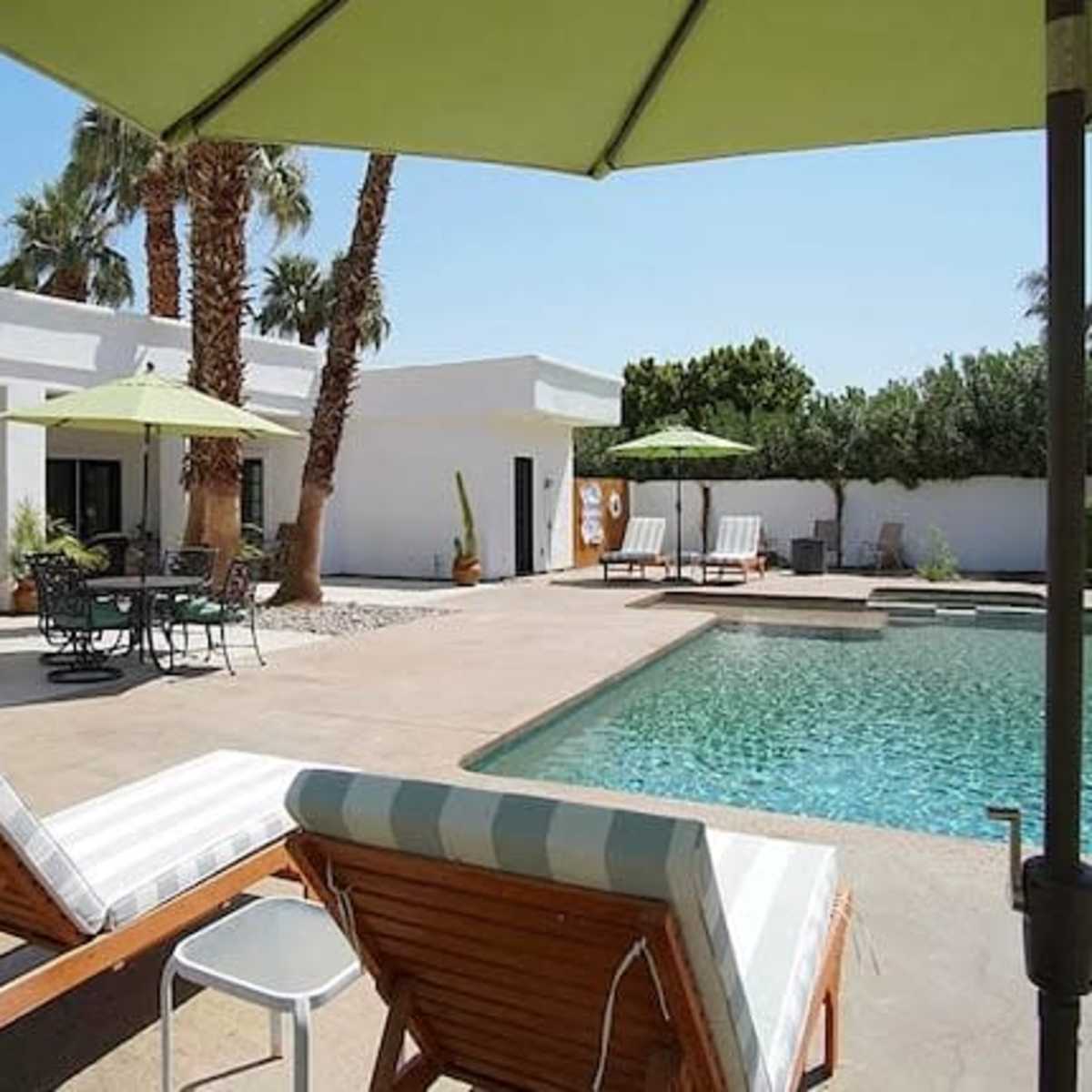 A backyard with a swimming pool, lounge chairs, and a small dining area under green umbrellas.