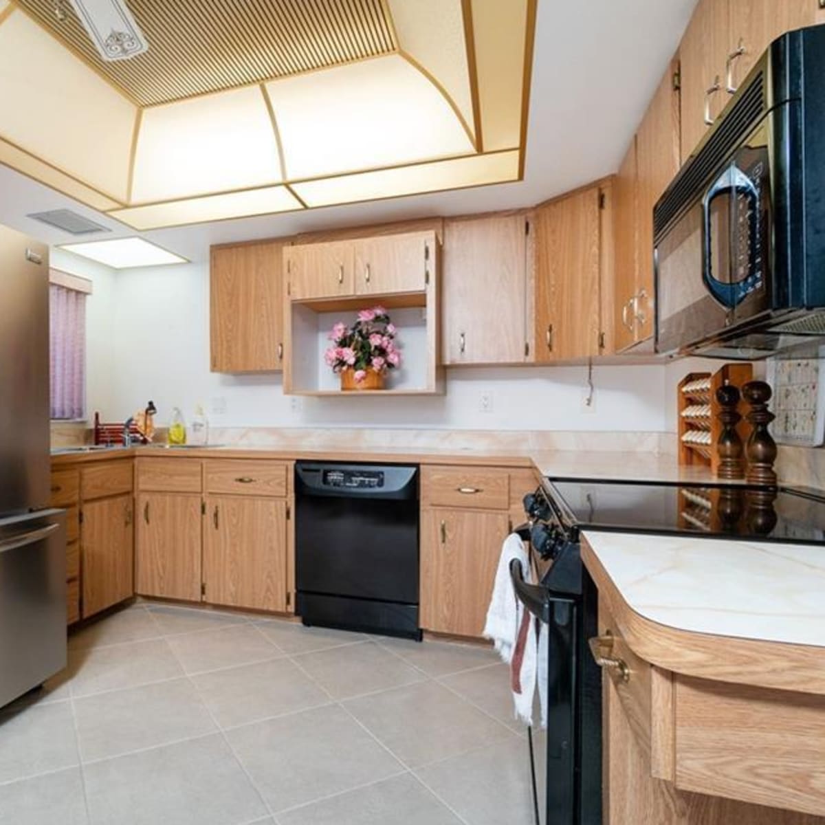 A kitchen with light wood cabinetry, a stainless steel refrigerator, a black dishwasher, and an oven with a microwave above it.