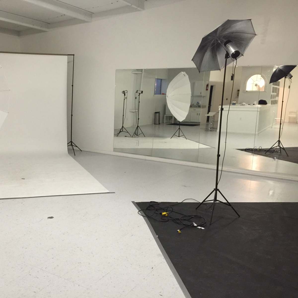 A photography studio with two large white umbrella lights, a backdrop, and mirrors reflecting the setup.