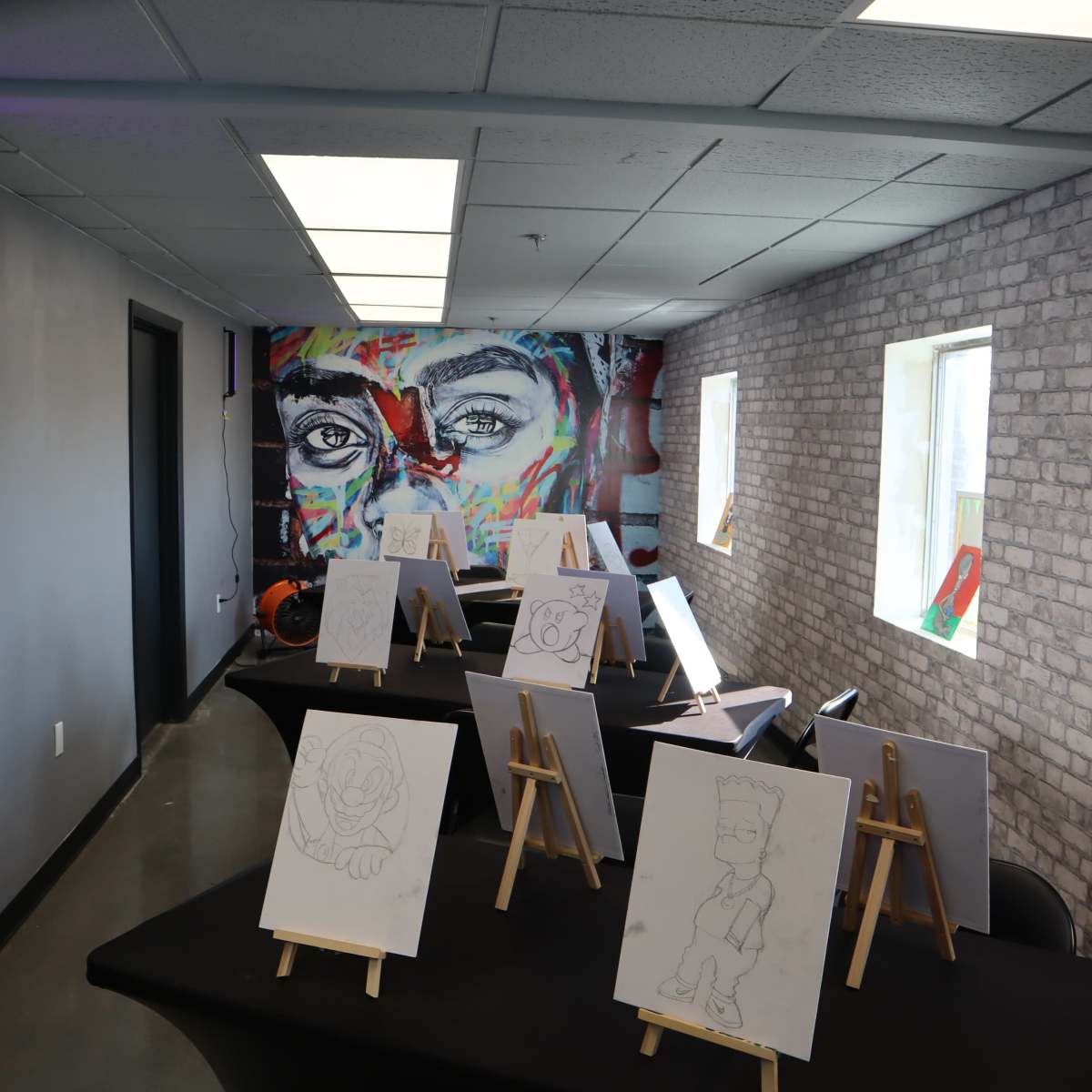 A creative workspace with several easels displaying sketches, set against a colorful mural of eyes on the wall.