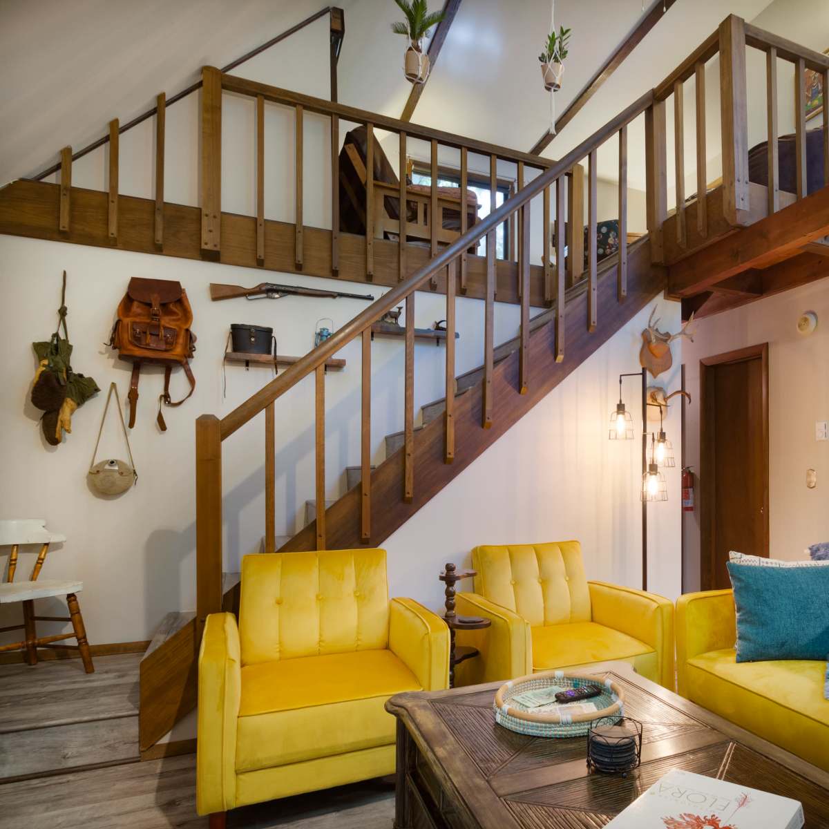 A cozy interior with a wooden staircase leading to an upper level, yellow couches, and a kitchen area featuring light blue cabinets.
