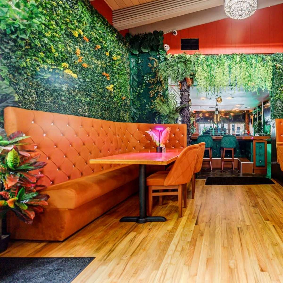 A vibrant restaurant interior featuring orange booths, wooden flooring, and a wall covered in greenery.