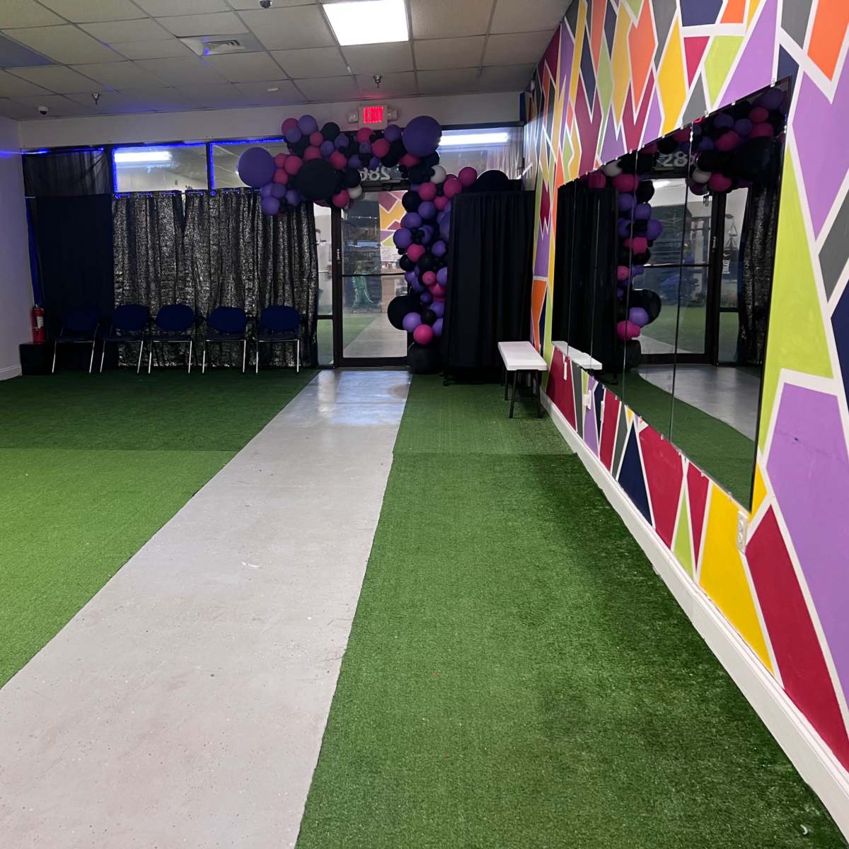 A large room with green turf flooring, a concrete pathway running through the center, and colorful walls decorated with geometric patterns.