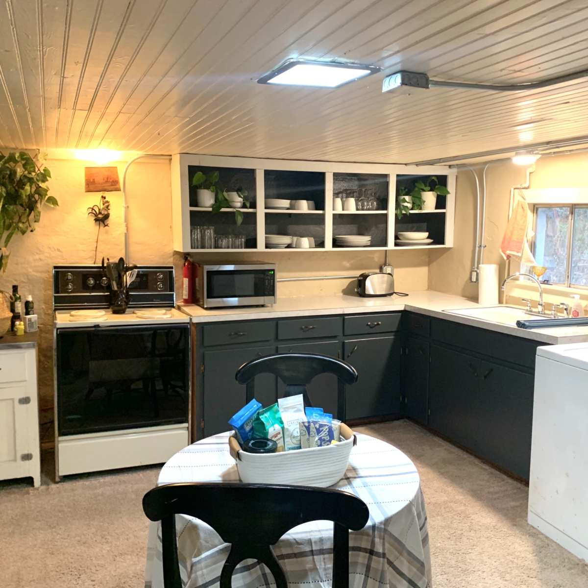 A cozy kitchen with white and dark cabinetry, appliances including a microwave and fridge, a round table set in the center, and a laundry area.