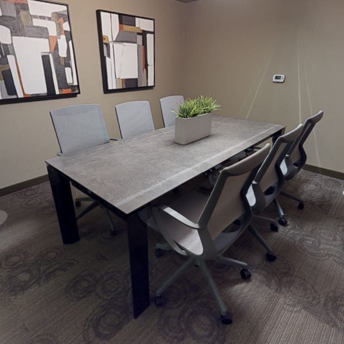 A conference room with a large table surrounded by six ergonomic chairs and two abstract artworks on the walls.