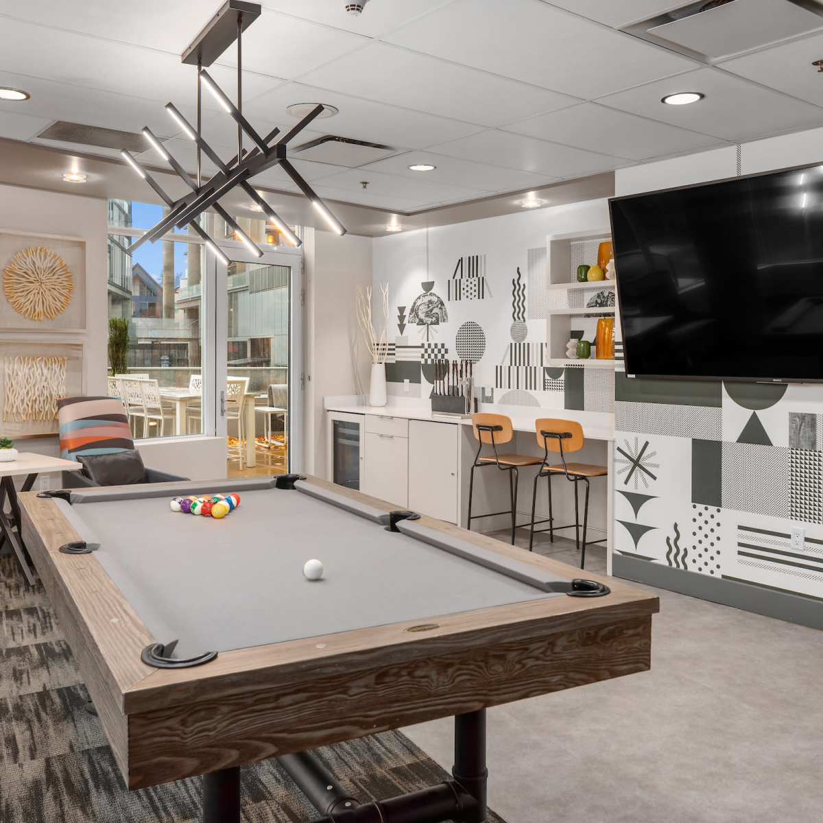 A modern game room featuring a pool table, seating area, and a large wall-mounted television with a patterned mural.