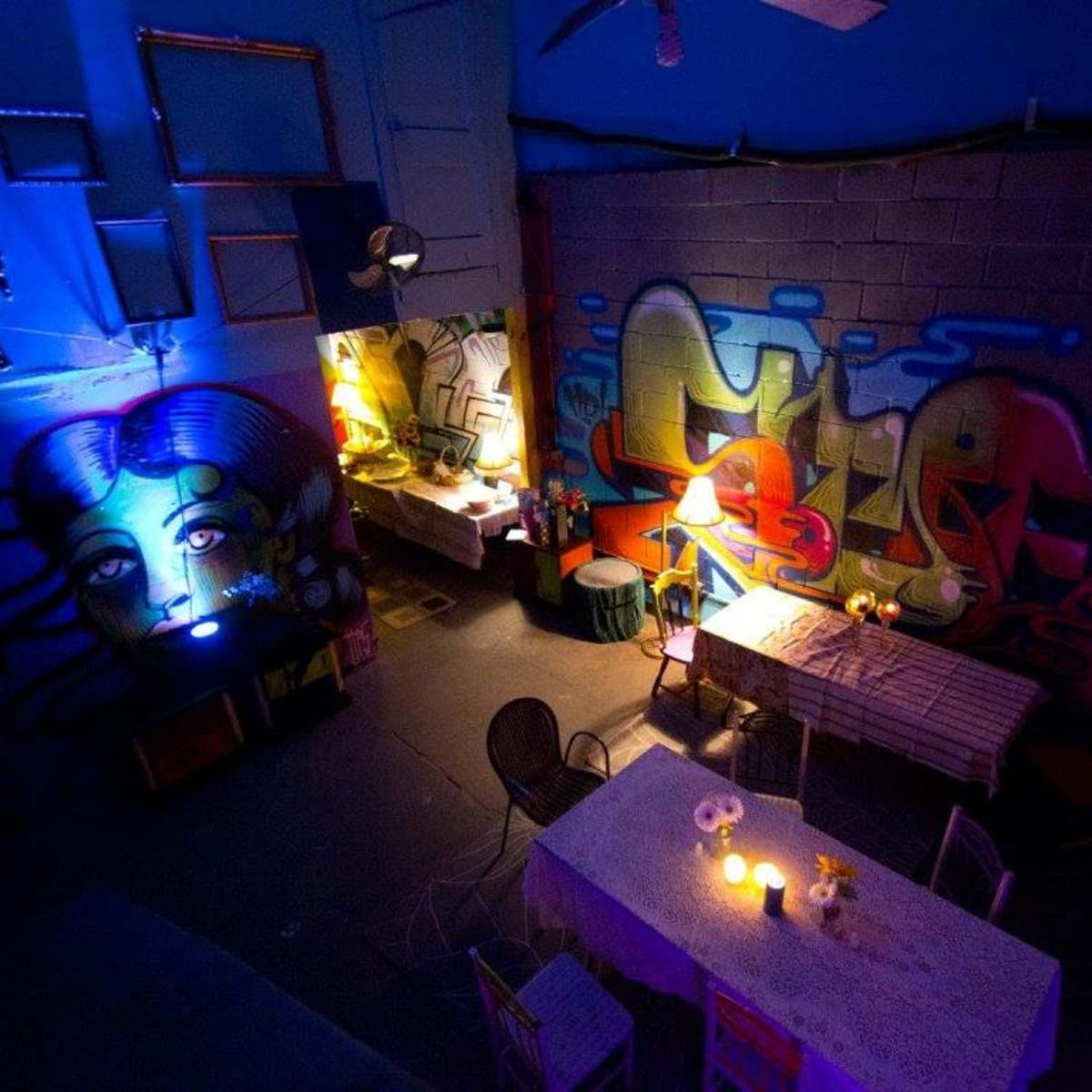An indoor space with colorful graffiti on the walls and two tables set with candles and flowers under dim lighting.