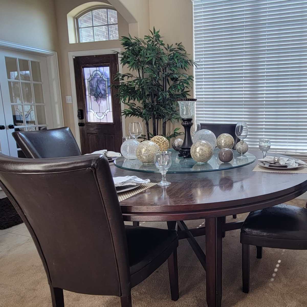 A dining area with a round wooden table set for a meal, surrounded by four black chairs, and decorated with spherical centerpieces and a side cabinet against the wall.