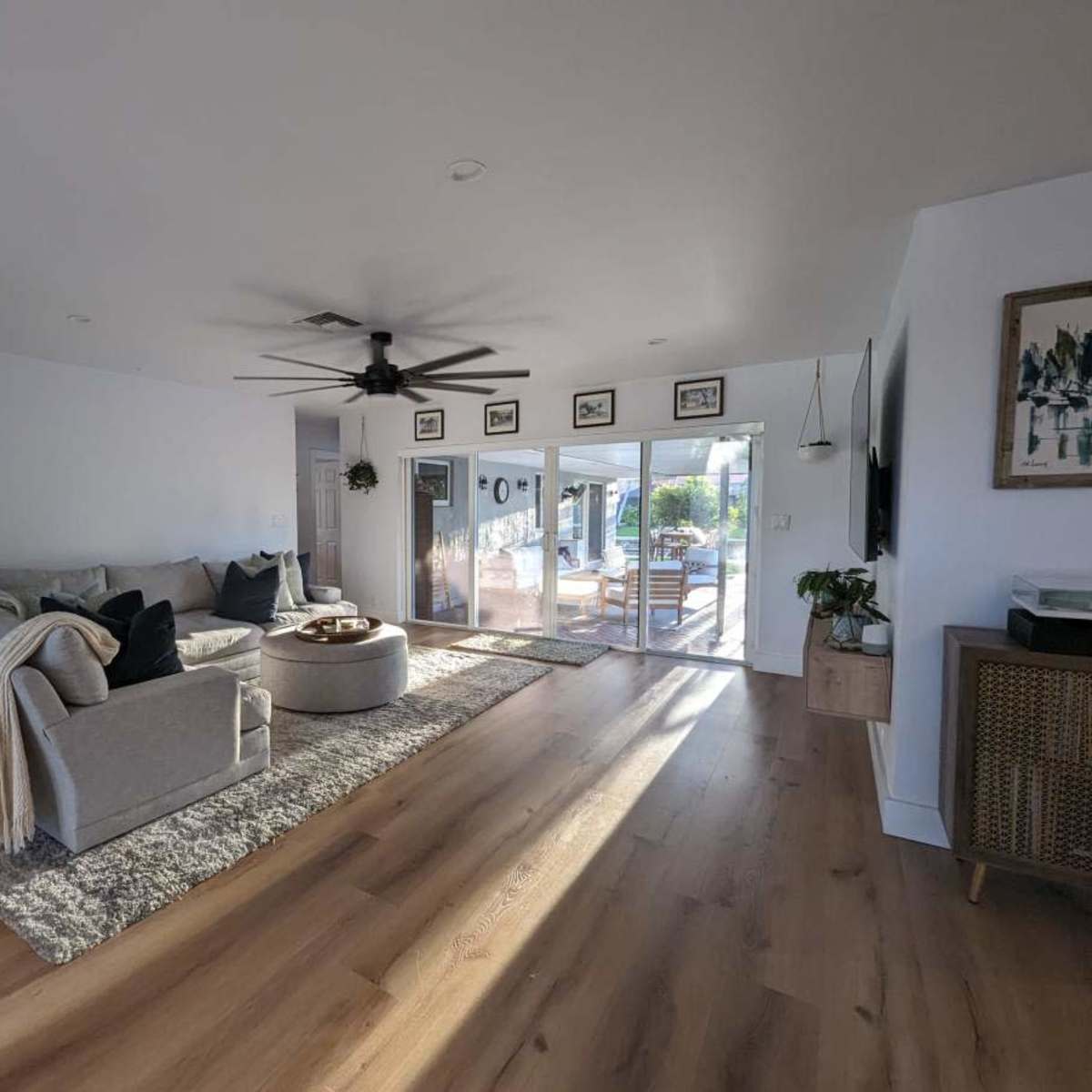 A modern living room with a large gray sectional sofa, a round coffee table, and sliding glass doors that open to an outdoor area.