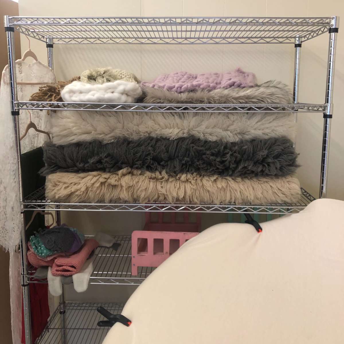 A wire shelving unit holds several stacked blankets and fabric items in a storage room.