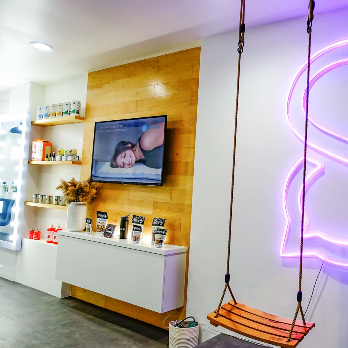 A modern interior of a spa or wellness center featuring a swinging seat, a television displaying a relaxing image, and a large illuminated letter "S" on the wall.