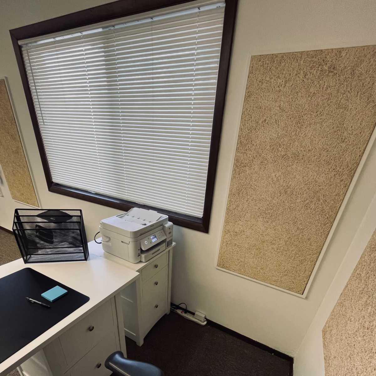 A neatly organized office corner with a printer on a white desk, a black chair, and two windows with blinds.