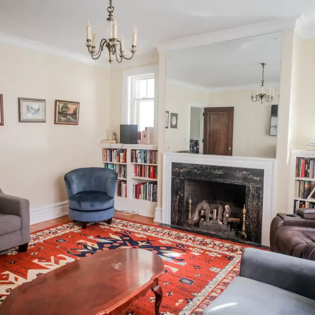 A living room with a patterned rug, two sofas, an armchair, a wooden coffee table, and a fireplace with a large mirror above it.