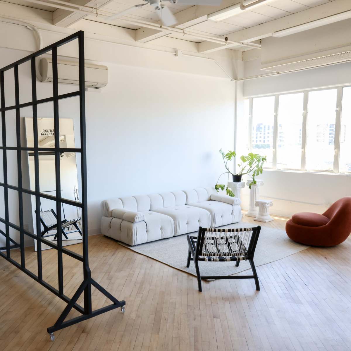 A spacious, well-lit room with modern furniture, including a white sofa, an orange chair, and a partition with a grid design.