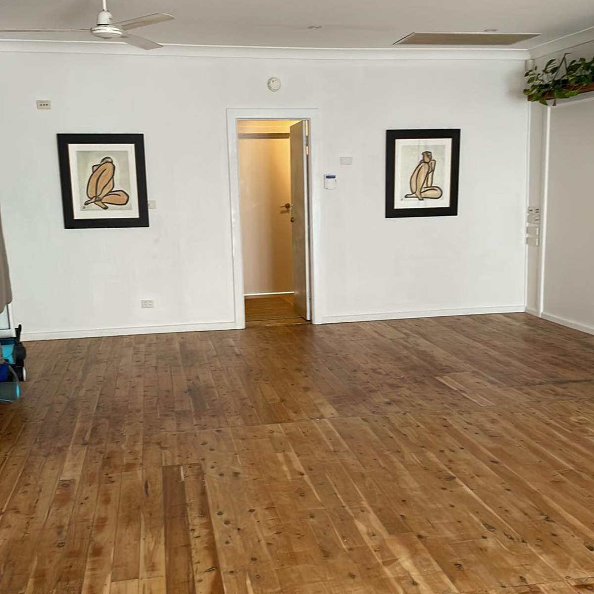 A spacious room with wooden flooring, two framed pictures on the wall, and a door leading to another area.