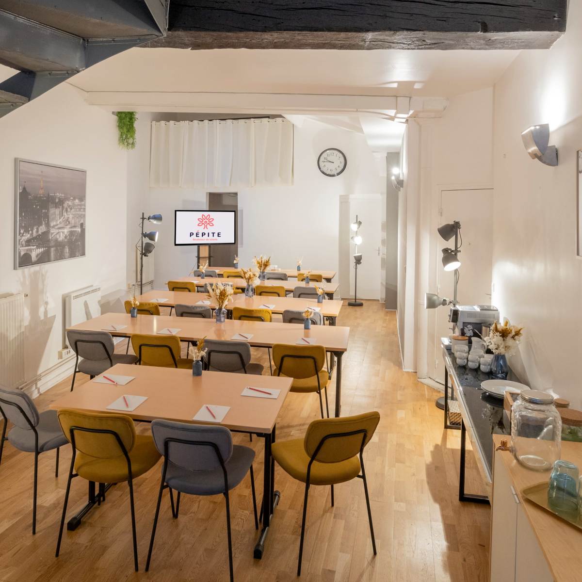 A well-organized meeting room features multiple tables set with chairs, a presentation screen, and a coffee station in the background.