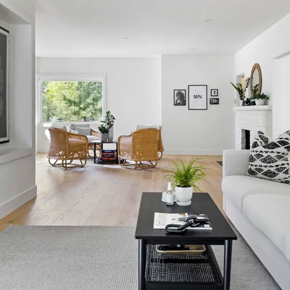 A modern living room features a light-colored sofa, a black coffee table, and wicker chairs arranged around a bright window.