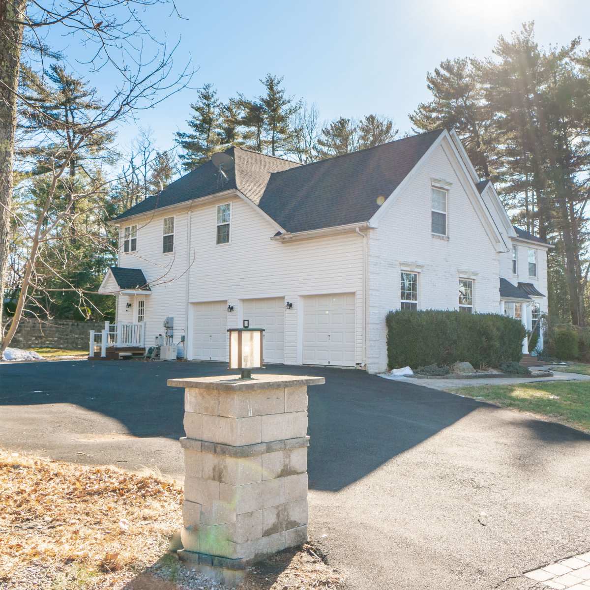 A large, white two-story house surrounded by trees and a paved driveway with stone lampposts at the entrance.