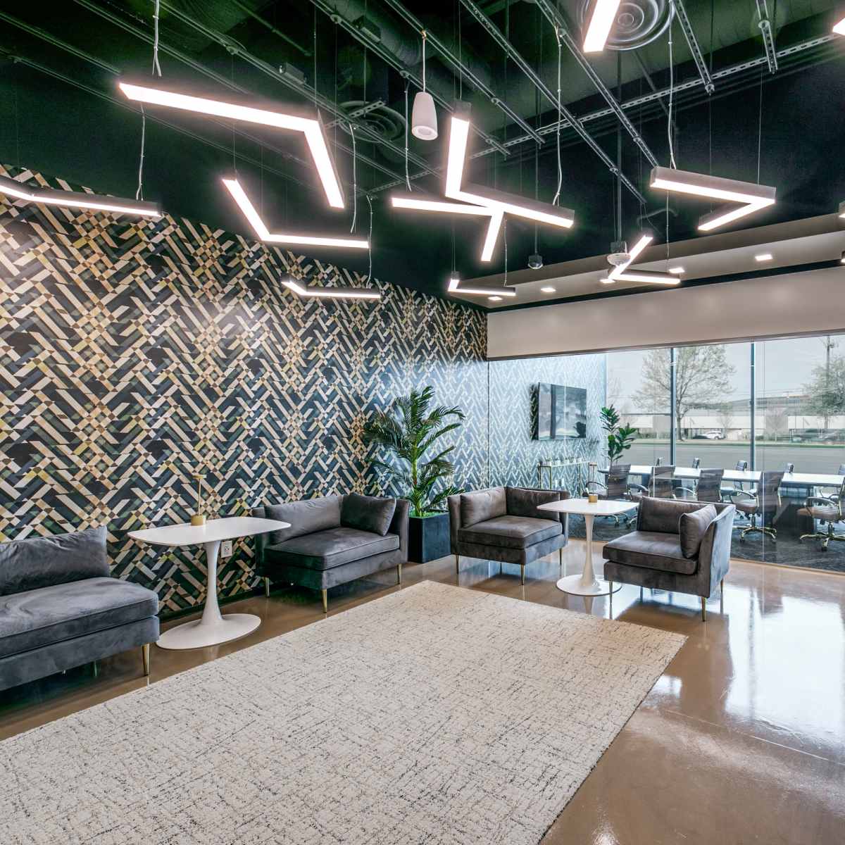 A modern office lounge area with stylish furniture, a patterned accent wall, and contemporary lighting.