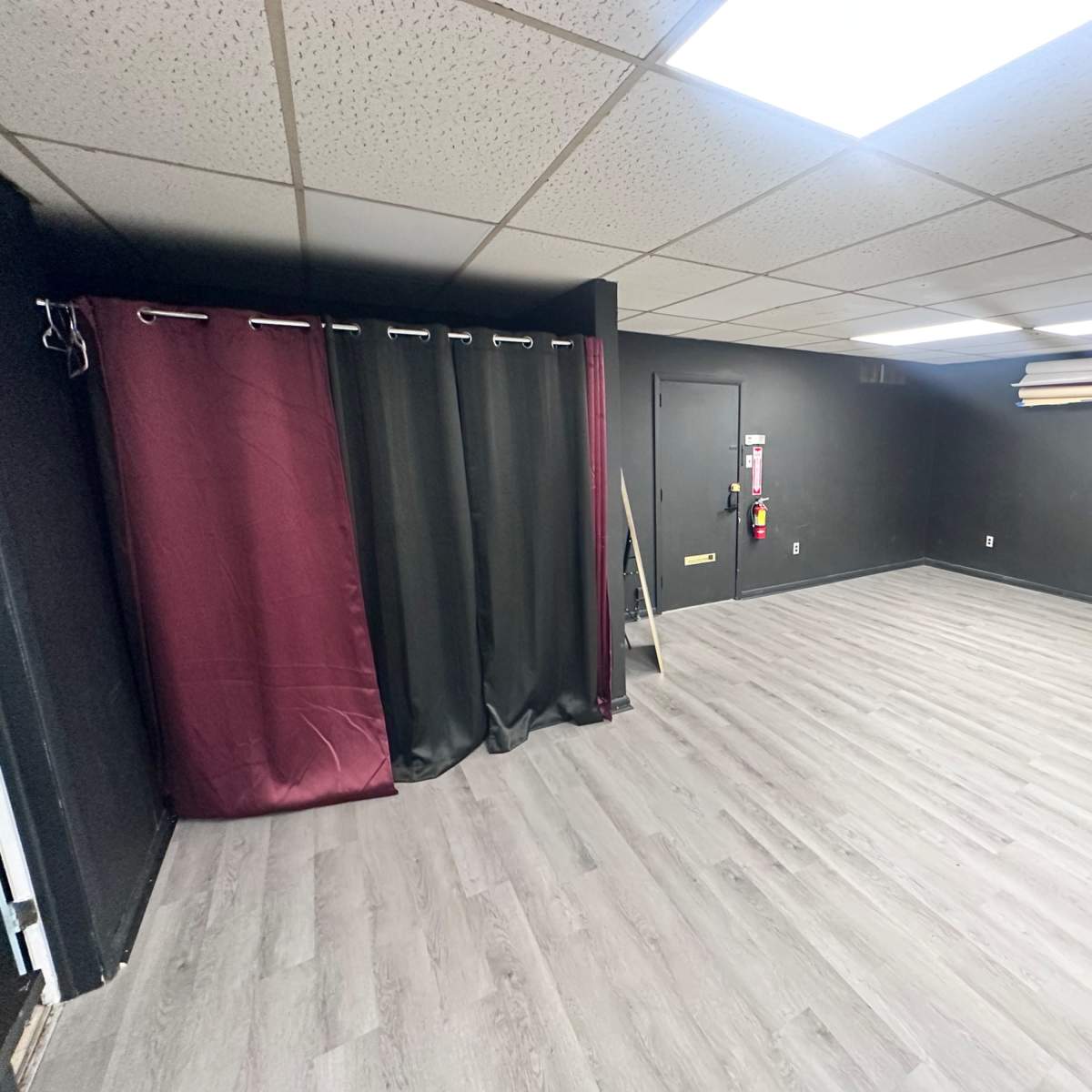 A spacious room with black walls, a dark curtain hanging at one end, and gray flooring.
