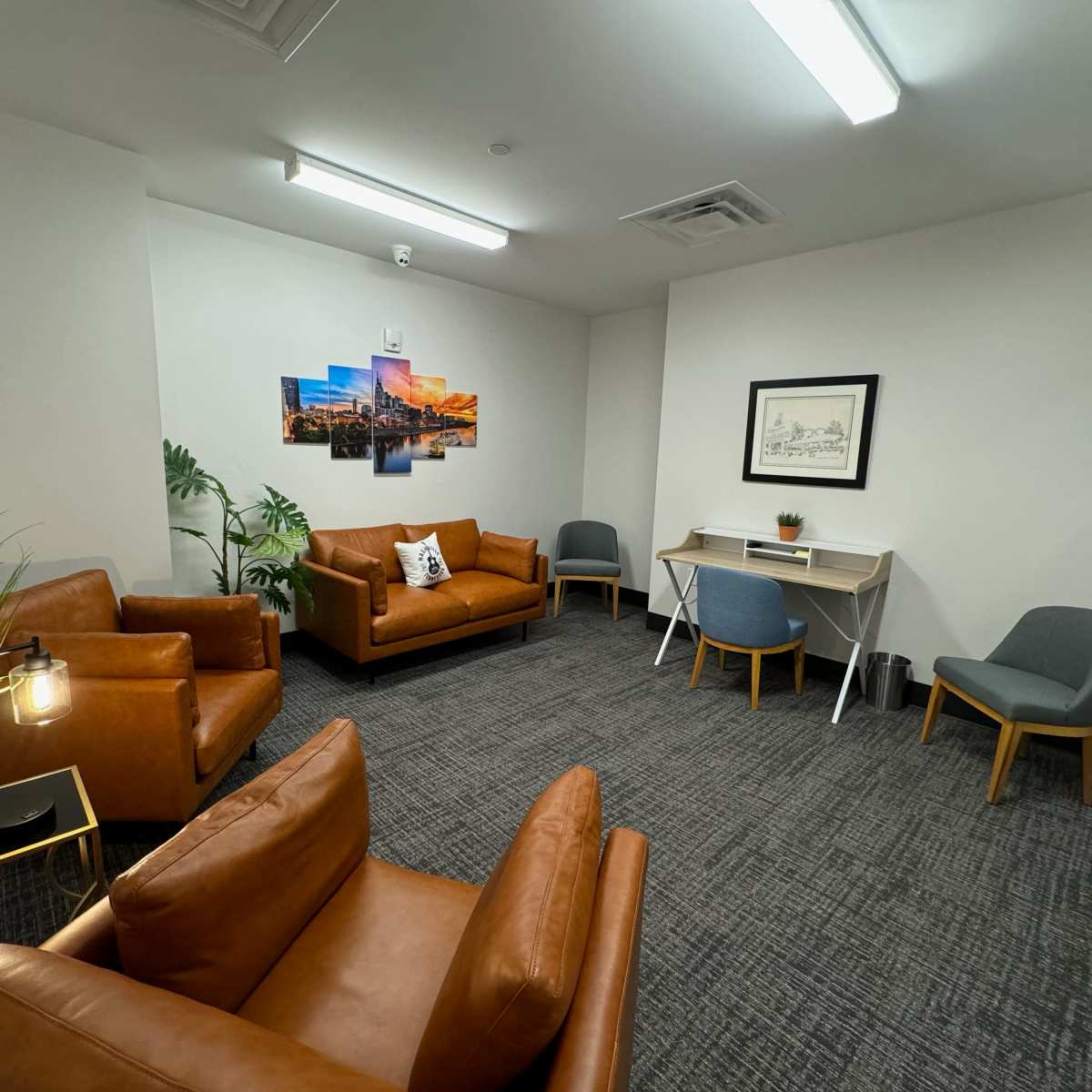 A modern interior lounge with brown leather chairs, a small desk, and decorative wall art in a well-lit room.