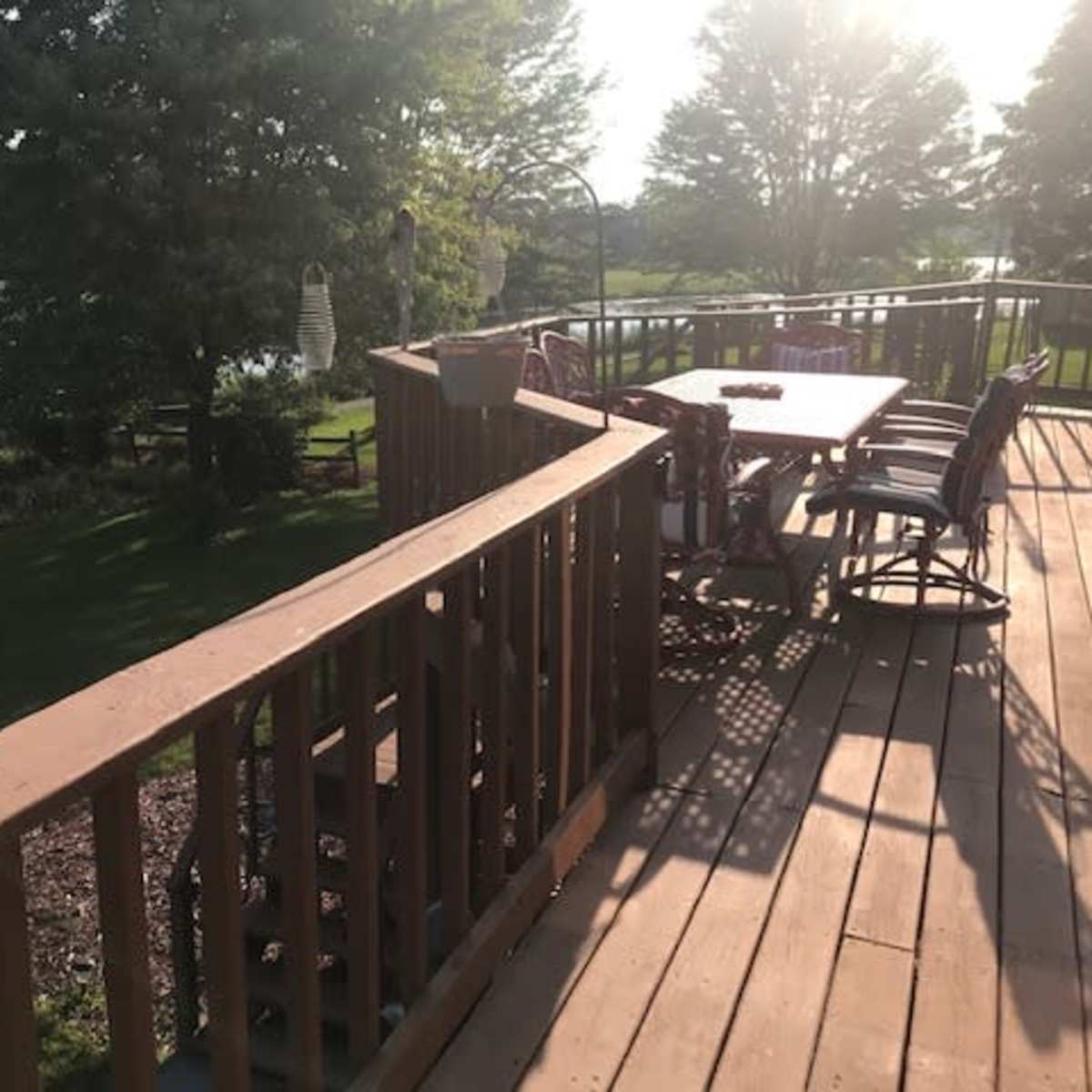 A wooden deck with a table and chairs overlooks a pond surrounded by greenery.