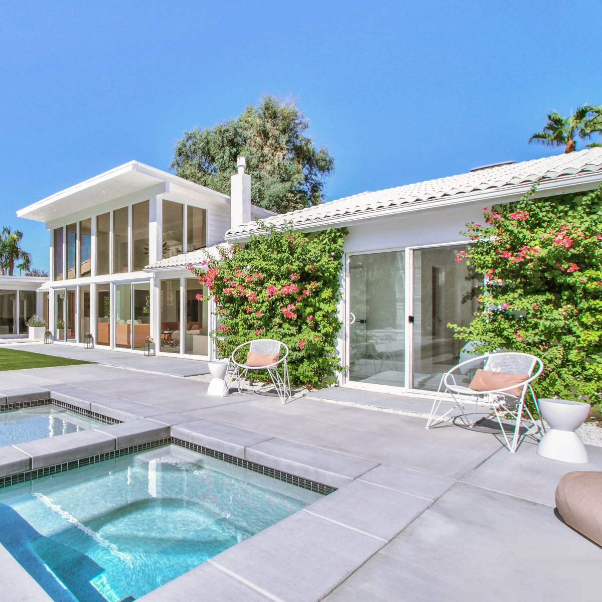 A modern house features a swimming pool and spa, surrounded by lush landscaping and bright blue skies.
