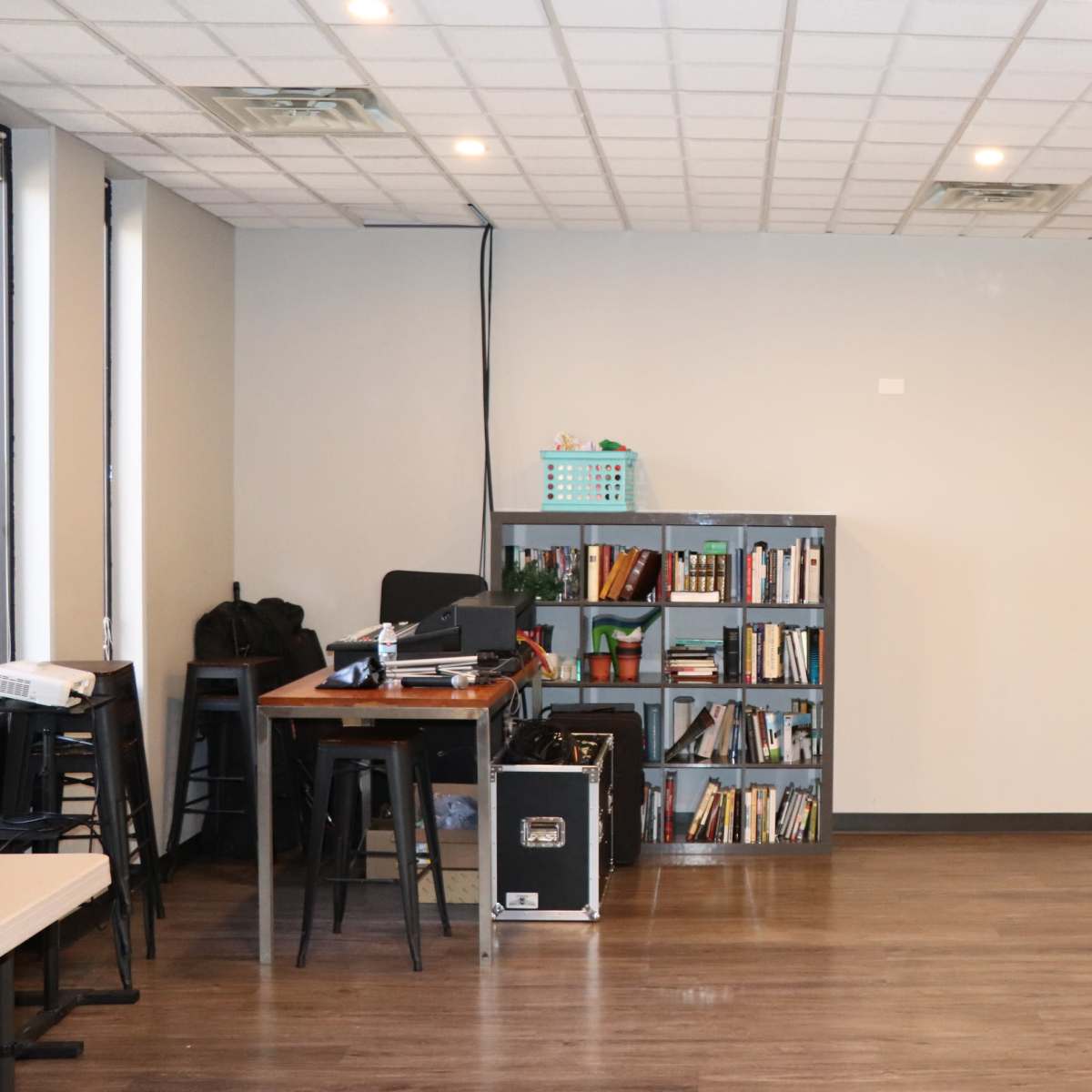 A room with a bookshelf, a small table, and a door, featuring hardwood floors and a drop ceiling.