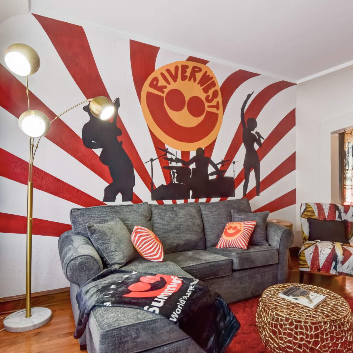 A living room with a gray couch, a floor lamp, a vibrant mural featuring silhouettes of musicians, and colorful decorative elements.