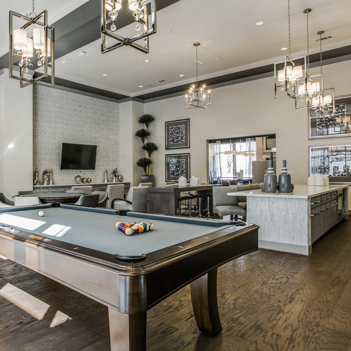 A modern game room featuring a pool table, stylish lighting fixtures, and a mix of seating areas with decorative plants.