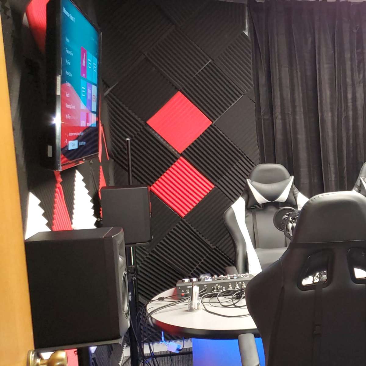 A soundproof recording studio with three chairs, microphone setups, and black and red diamond-patterned acoustic panels on the walls.