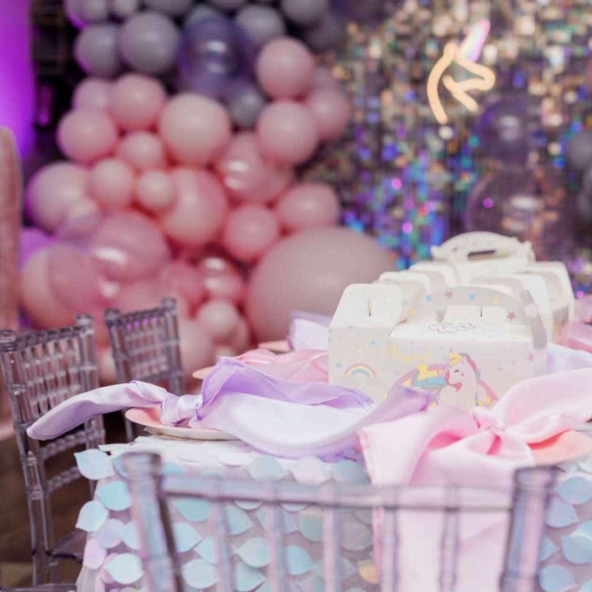 A decorated table for a celebration, featuring a pastel balloon backdrop, gift boxes, and colored table settings.