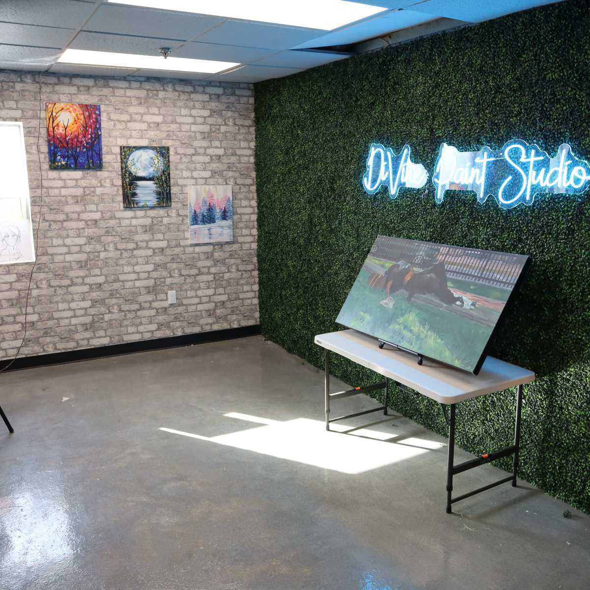 The scene shows a cozy art studio featuring a green, textured wall, a TV on a table, and several artworks displayed in frames.