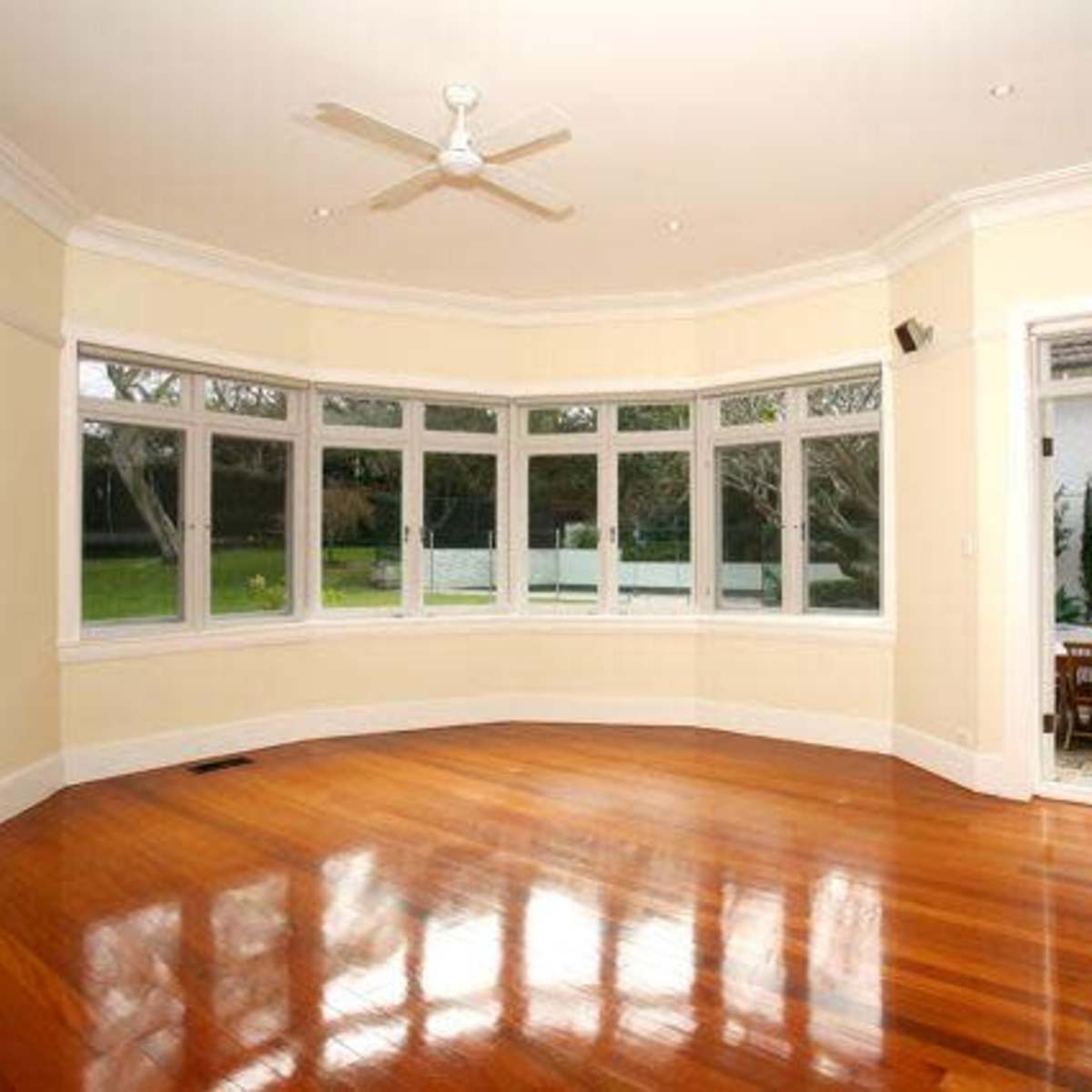 A spacious living room with large windows, wooden flooring, and a view of an outdoor patio area.