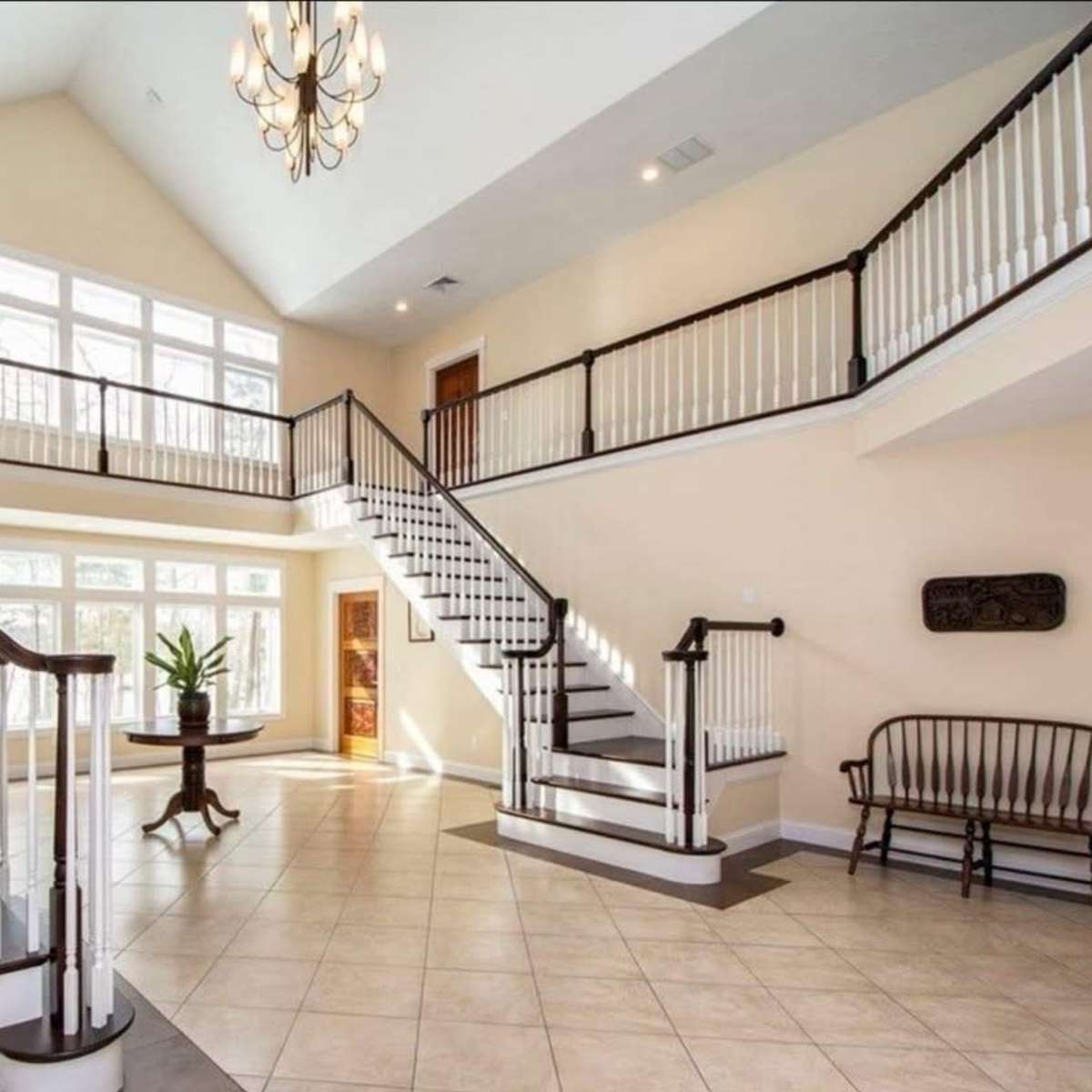 A spacious two-story entryway with large windows, sweeping staircases, and a bench by the wall.
