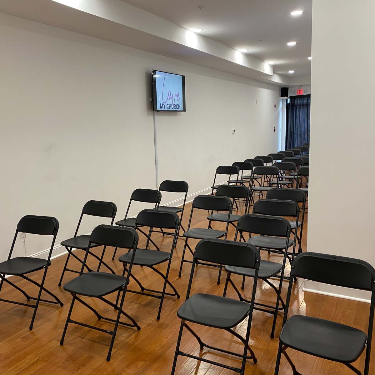 A room with rows of black folding chairs set up in front of a wall-mounted screen.