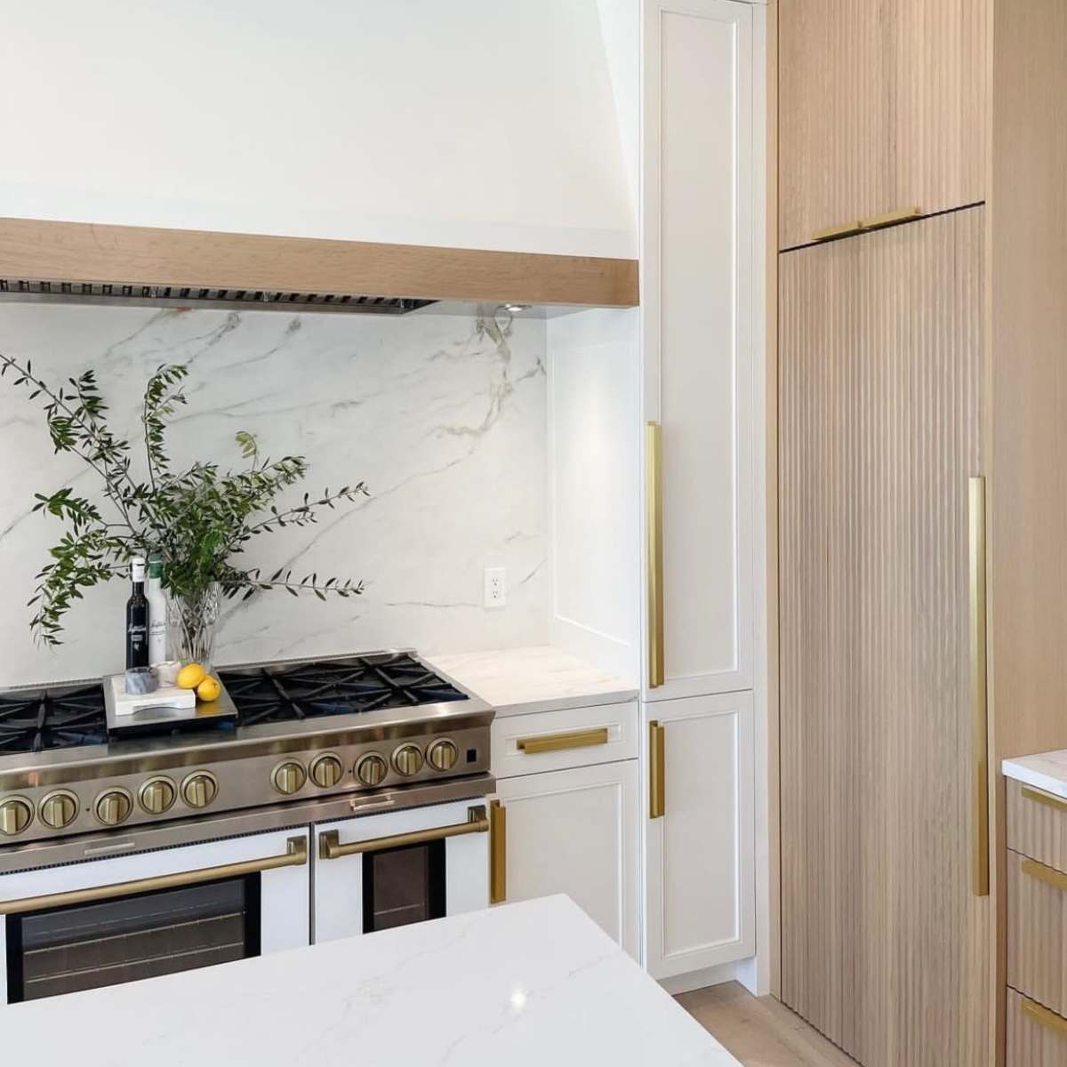 A modern kitchen with a stainless steel stove, a marble backsplash, and cabinetry featuring wood accents.