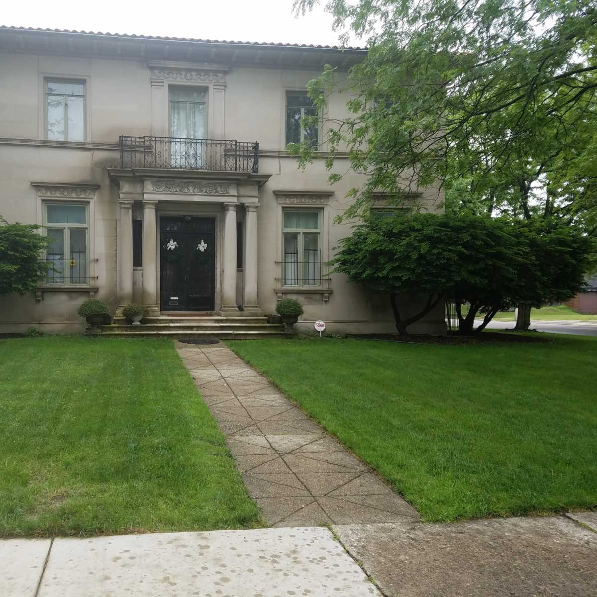 A large, two-story house with a symmetrical facade, a central staircase, and manicured shrubs flanking the entrance.