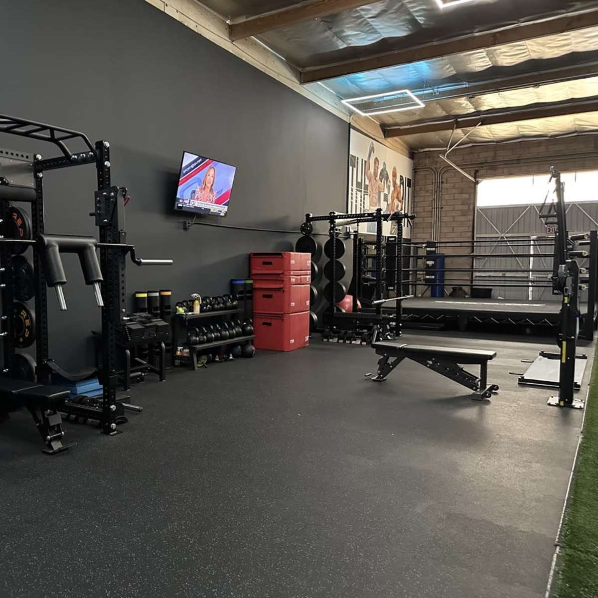 A well-equipped gym space featuring weightlifting equipment, benches, and a television mounted on the wall.