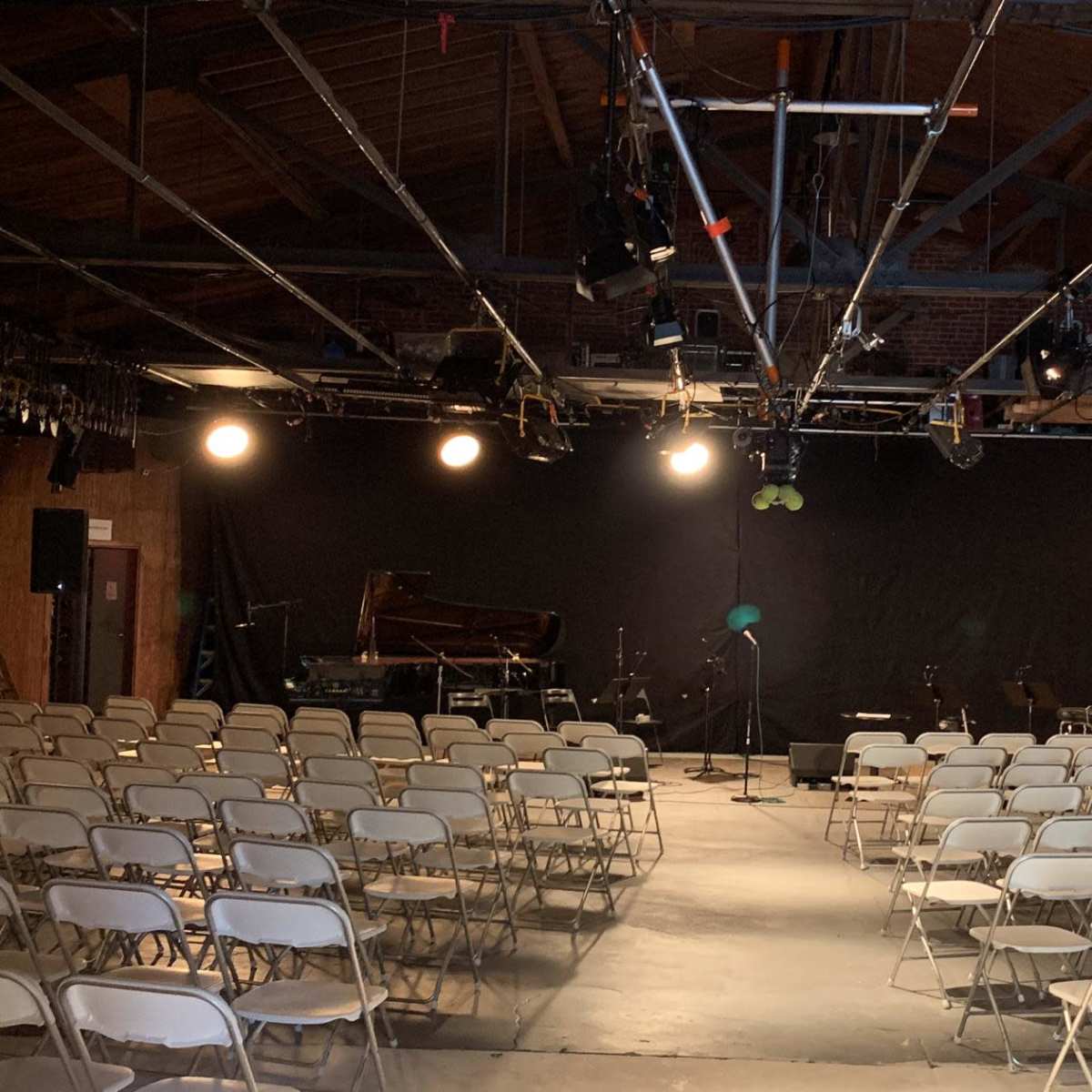 A concert venue with rows of white chairs facing a dark curtain and a stage equipped with a piano and musical instruments.