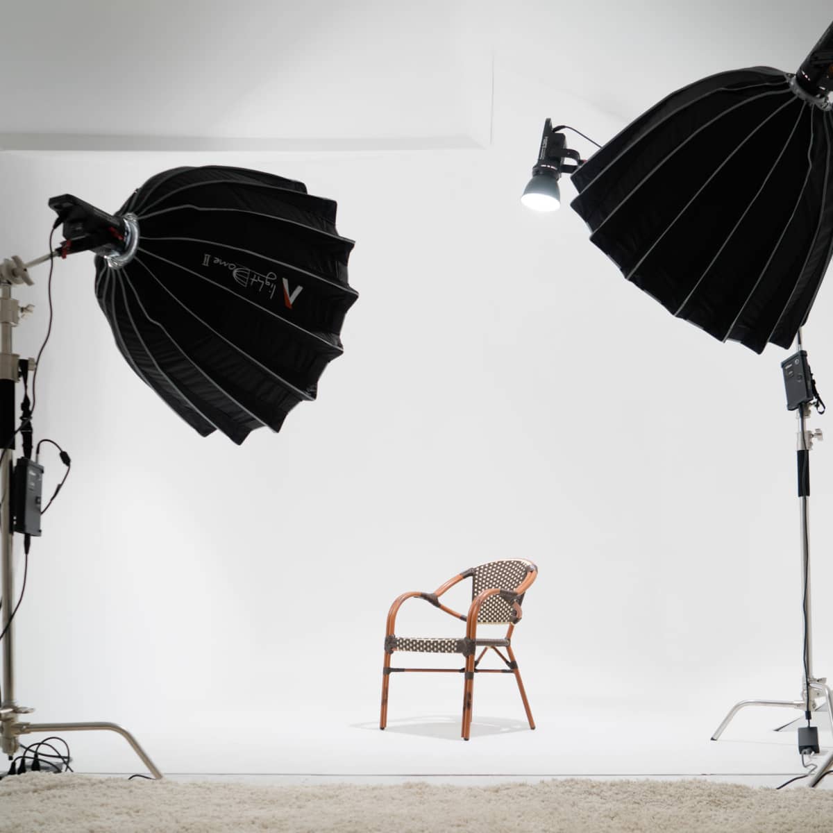 A photography studio is set up with two softbox lights illuminating an empty chair on a white backdrop.