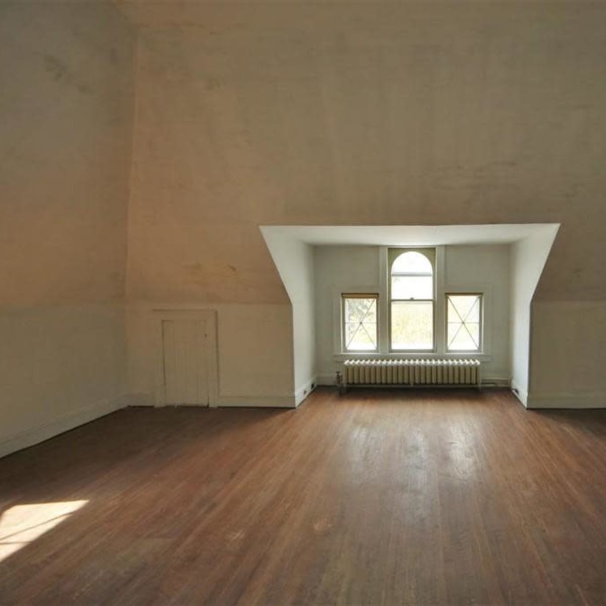 An empty room with a sloped ceiling features a large window and a wooden floor.