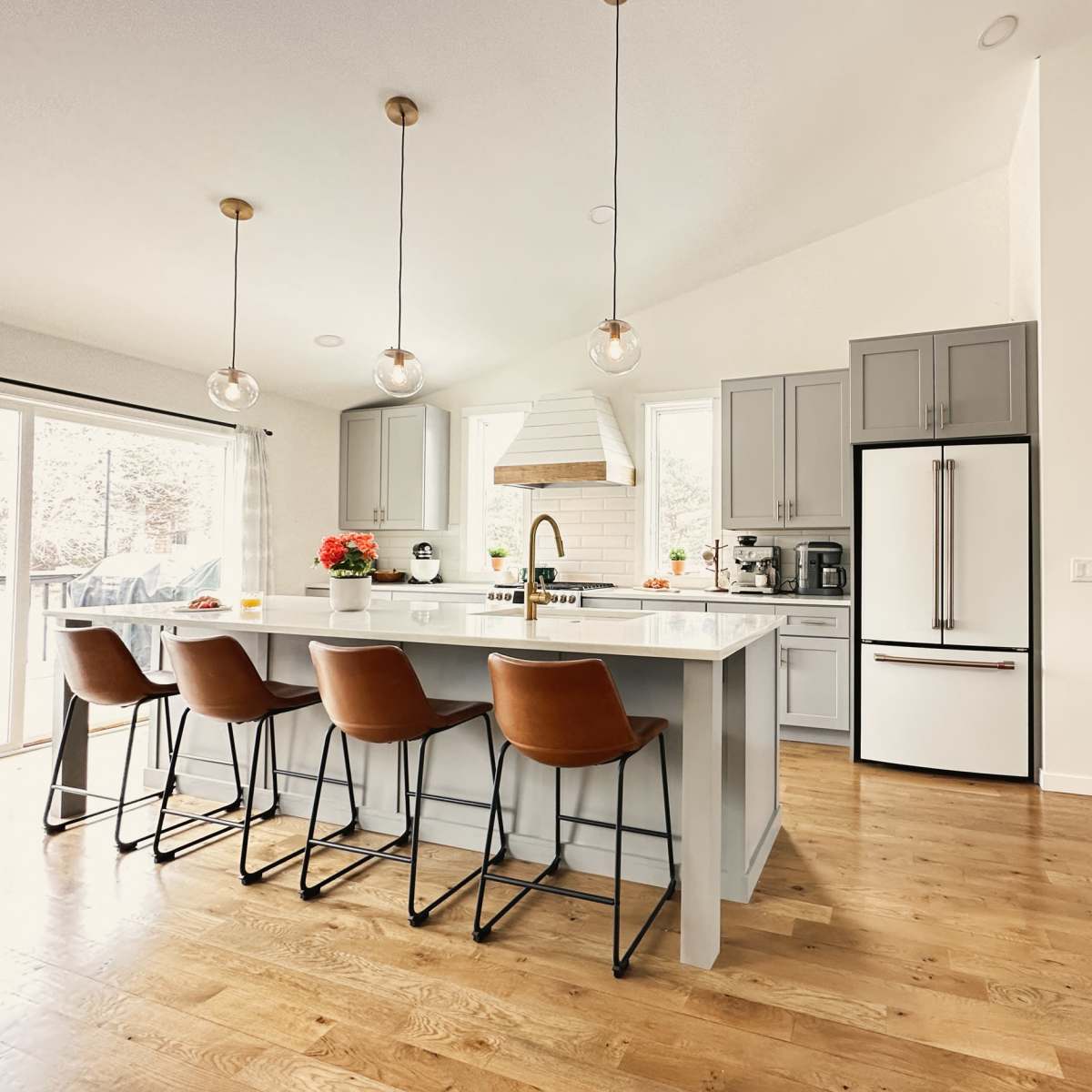 The kitchen features a large island with four bar stools, modern cabinetry, a refrigerator, and natural light from sliding glass doors.