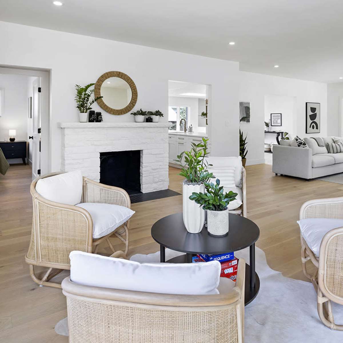 A bright, modern living room featuring two woven chairs positioned around a small black table, with a white stone fireplace in the background.